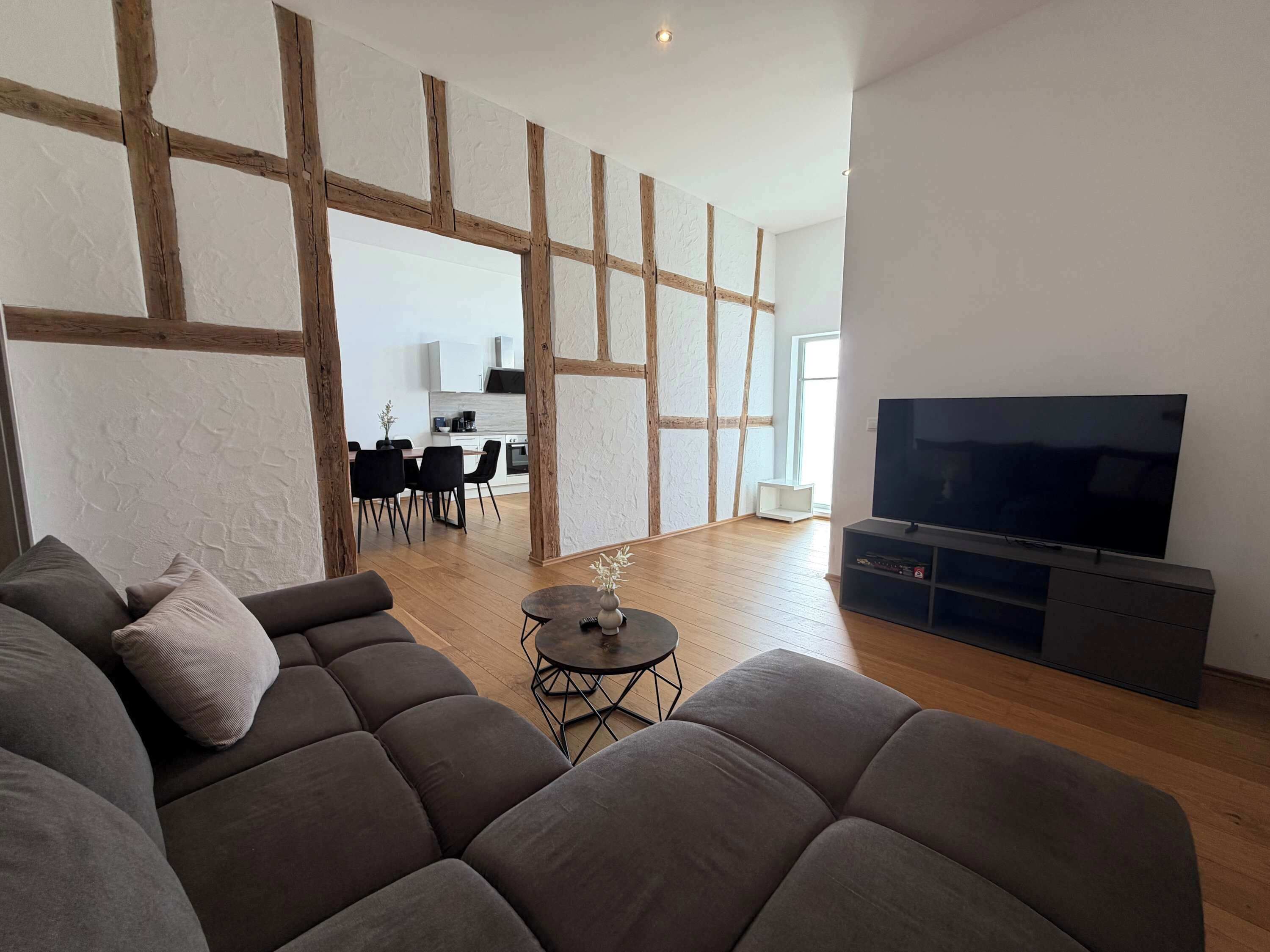 Een moderne woonkamer met een grote hoekbank, een klein rond tafeltje en een flatscreen televisie op een standaard.