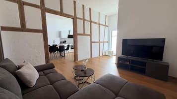 Een moderne woonkamer met een grote hoekbank, een klein rond tafeltje en een flatscreen televisie op een standaard.
