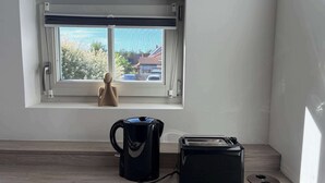 Ein Zimmer mit Fenster, einem Wasserkocher, einem Toaster und einer kleinen Figur am Fensterbrett.