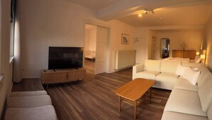 Sala de estar com televisão, sofá e piso de madeira.