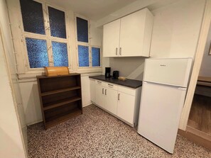 Una cocina compacta con armarios blancos, horno integrado y ventana con vidrio azulado.