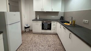 Cozinha compacta com armários brancos, bancada preta e piso estampado.