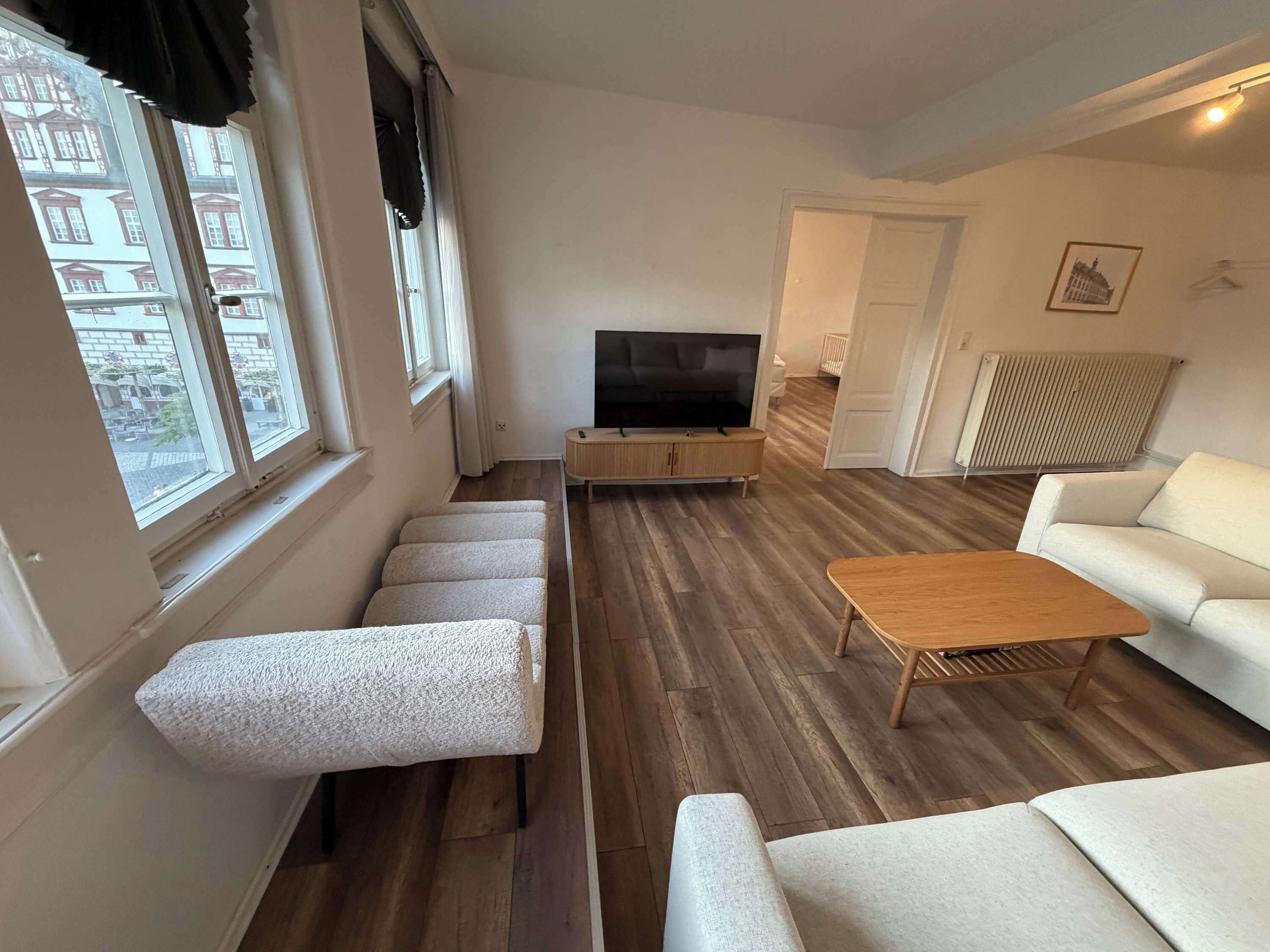 Een woonkamer met een bank, een salontafel, een tv op een dressoir en uitzicht door het raam.