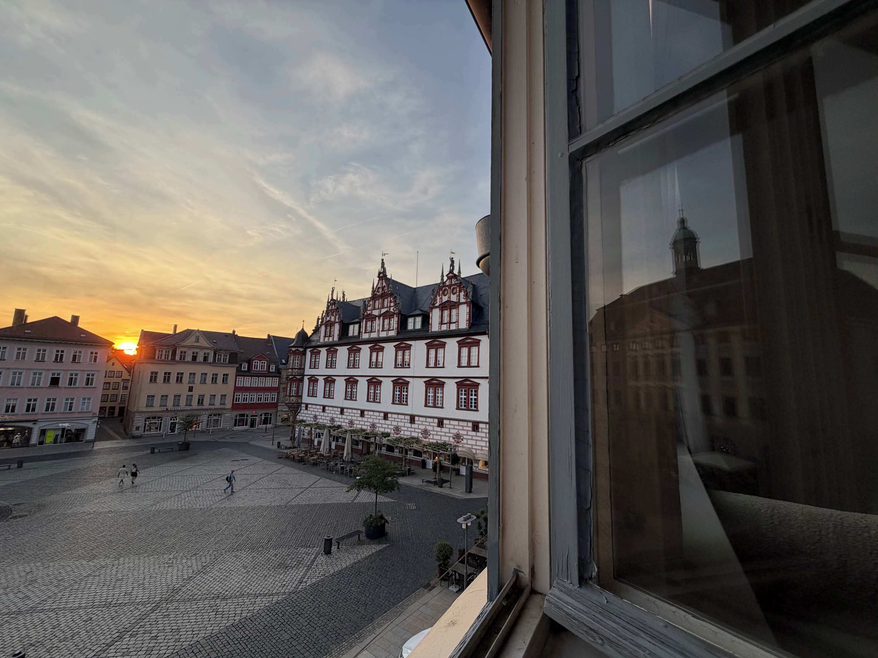 Una plaza empedrada con edificios históricos, cielo despejado y un atardecer.