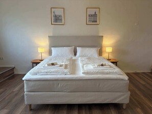 Un lit bien fait, avec du linge de lit et des serviettes blanches, deux lampes de chevet et deux tableaux encadrés accrochés au mur.