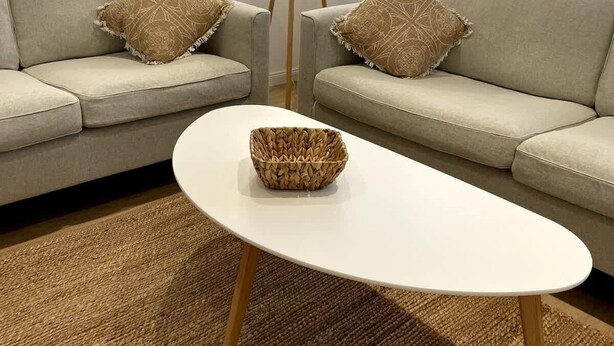 Un soggiorno con un divano, due cuscini decorativi, una lampada da terra e un tavolino da caffè in rattan.
