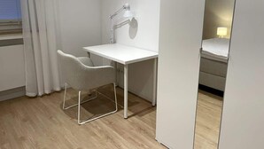 Una stanza piccola e moderna con una scrivania bianca, una sedia, una lampada da scrivania e uno specchio.