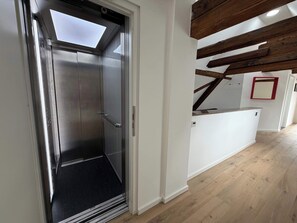 An elevator with a metallic finish, a black rubber mat at the bottom, and a white wall adjacent to it.