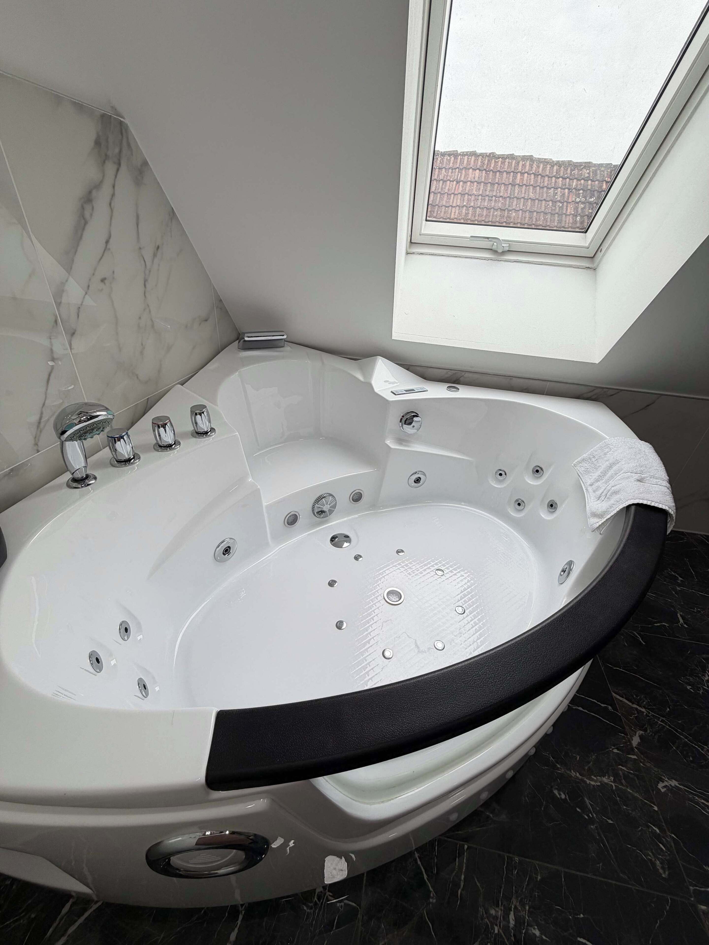A corner bathroom with a freestanding bathtub, a window, and a marble wall.