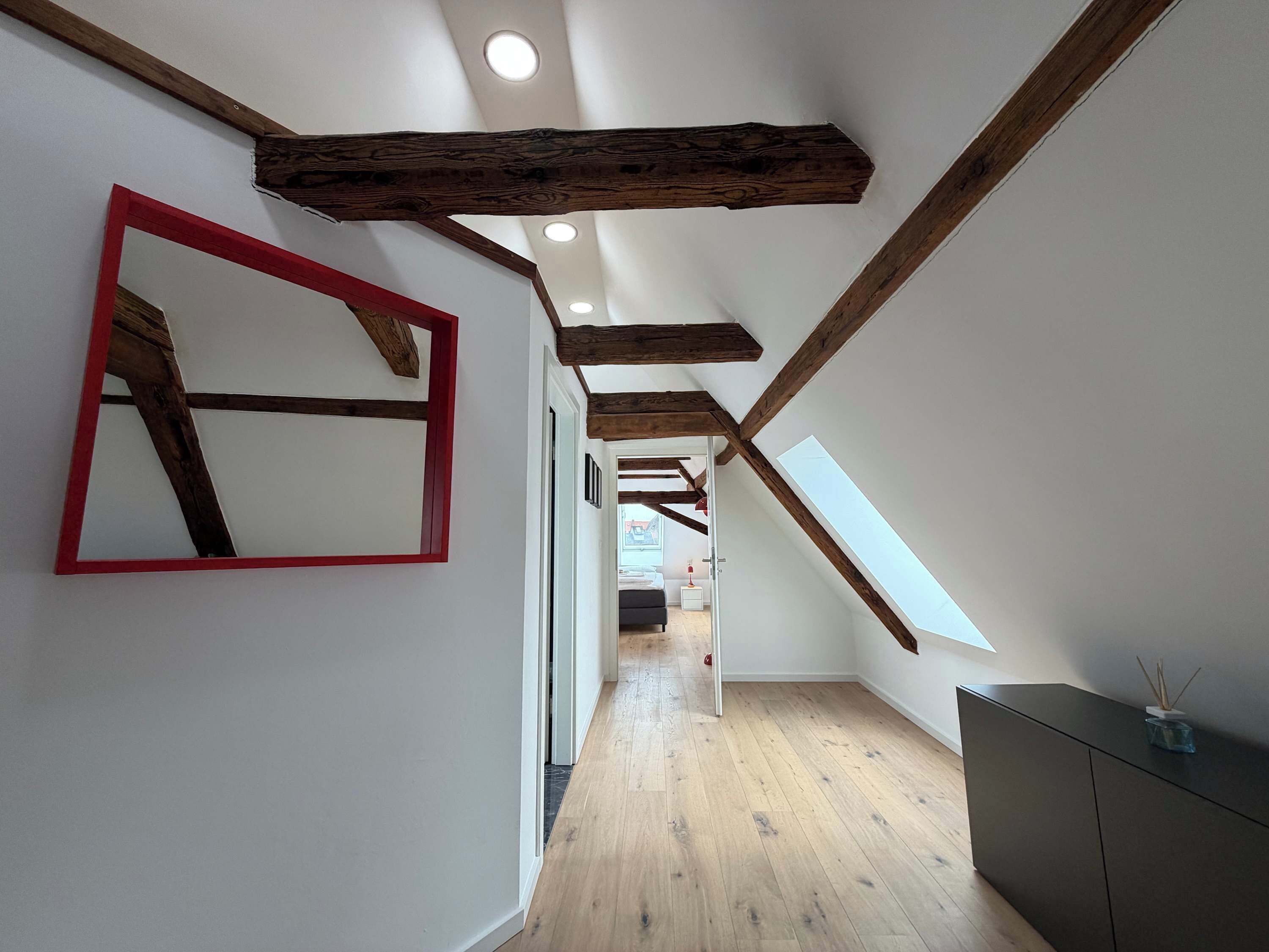 A hallway with wooden beams, a red-framed mirror, and a dark-toned cabinet.