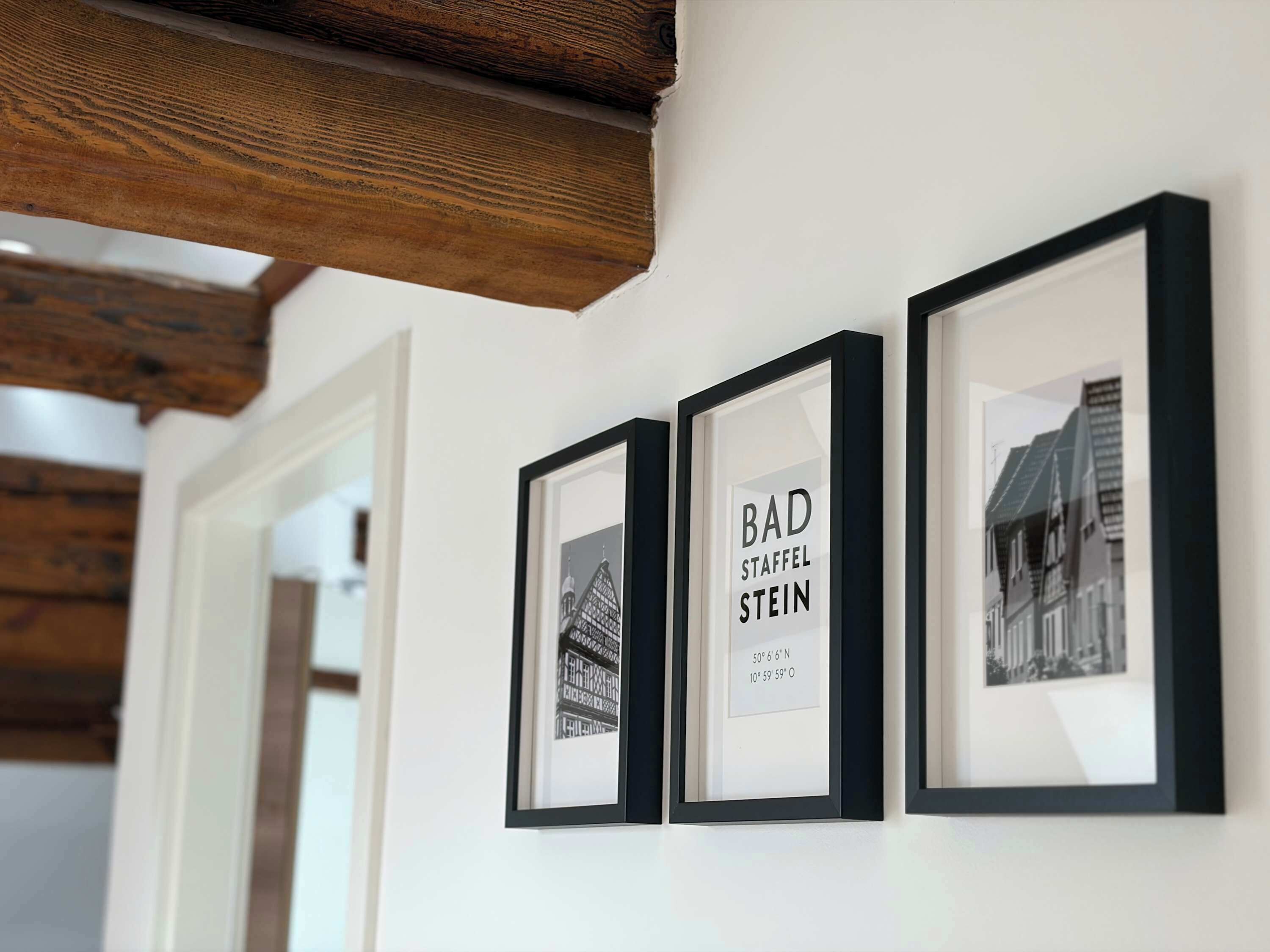 Drie ingelijste foto’s aan een muur, één met tekst en twee met gebouwen.