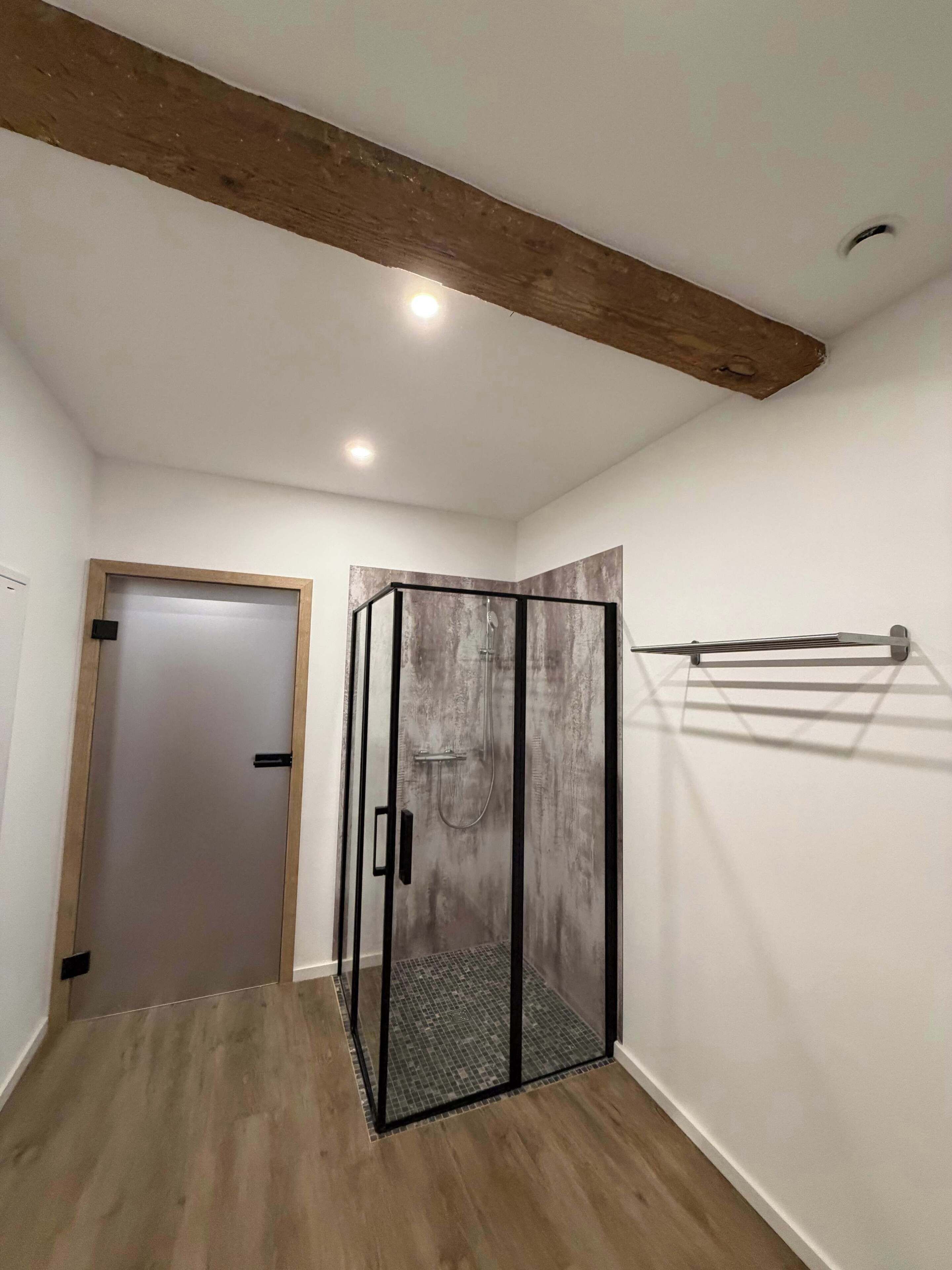 Ein Zimmer mit Holzboden, einer in Glas abgeschlossenen Dusche und Fliesenboden.