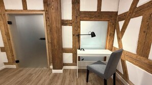 Um quarto com uma escrivaninha branca, uma cadeira cinzenta e um abajur preto.