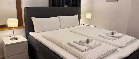 A neatly made bed with two pillows, a bedside lamp, and a folded towel on the nightstand.