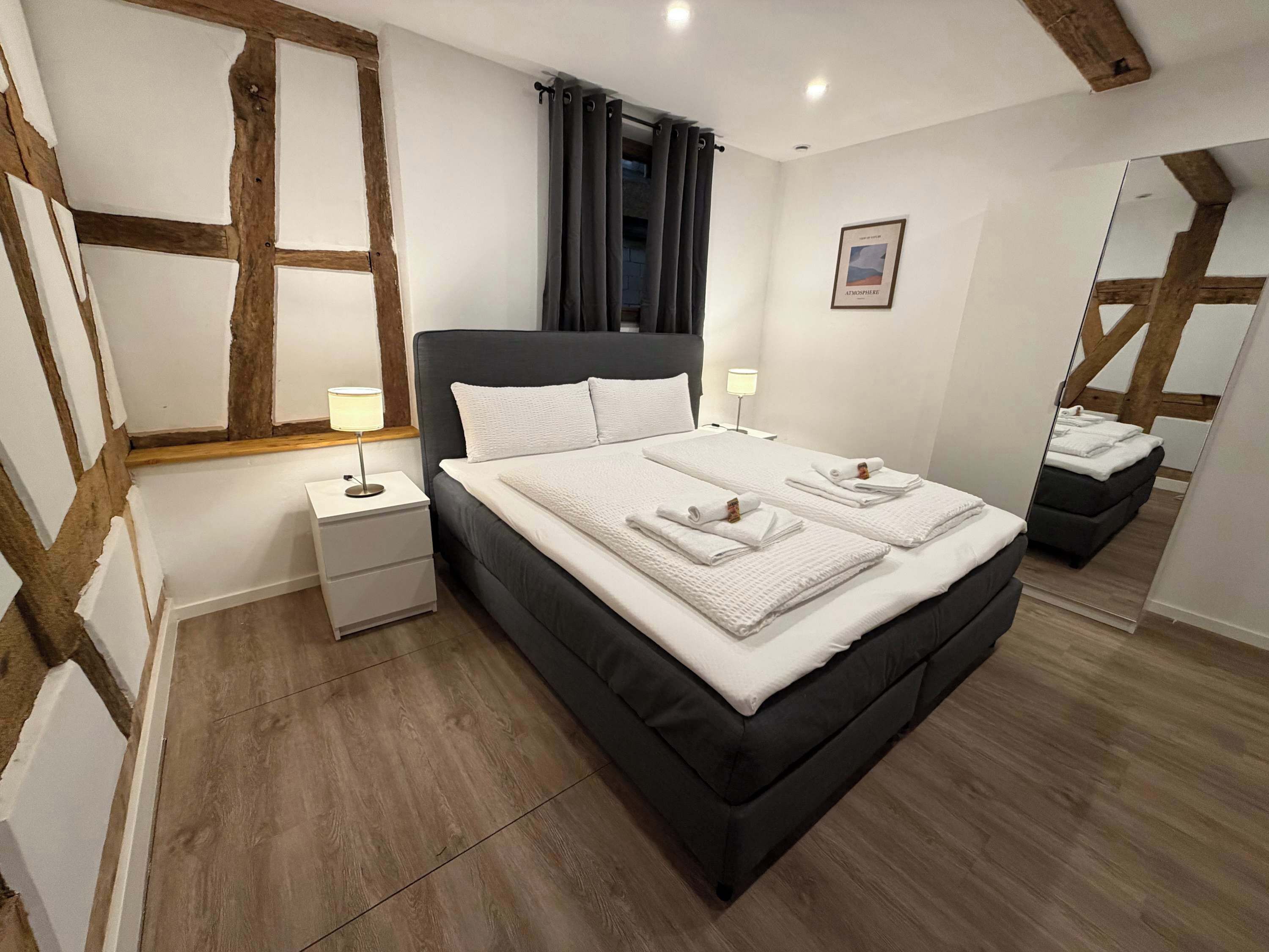 Een slaapkamer met een groot bed, twee nachtkastjes, een spiegel en een lijst met een afbeelding aan de muur.