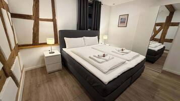 Een slaapkamer met een groot bed, twee nachtkastjes, een spiegel en een lijst met een afbeelding aan de muur.