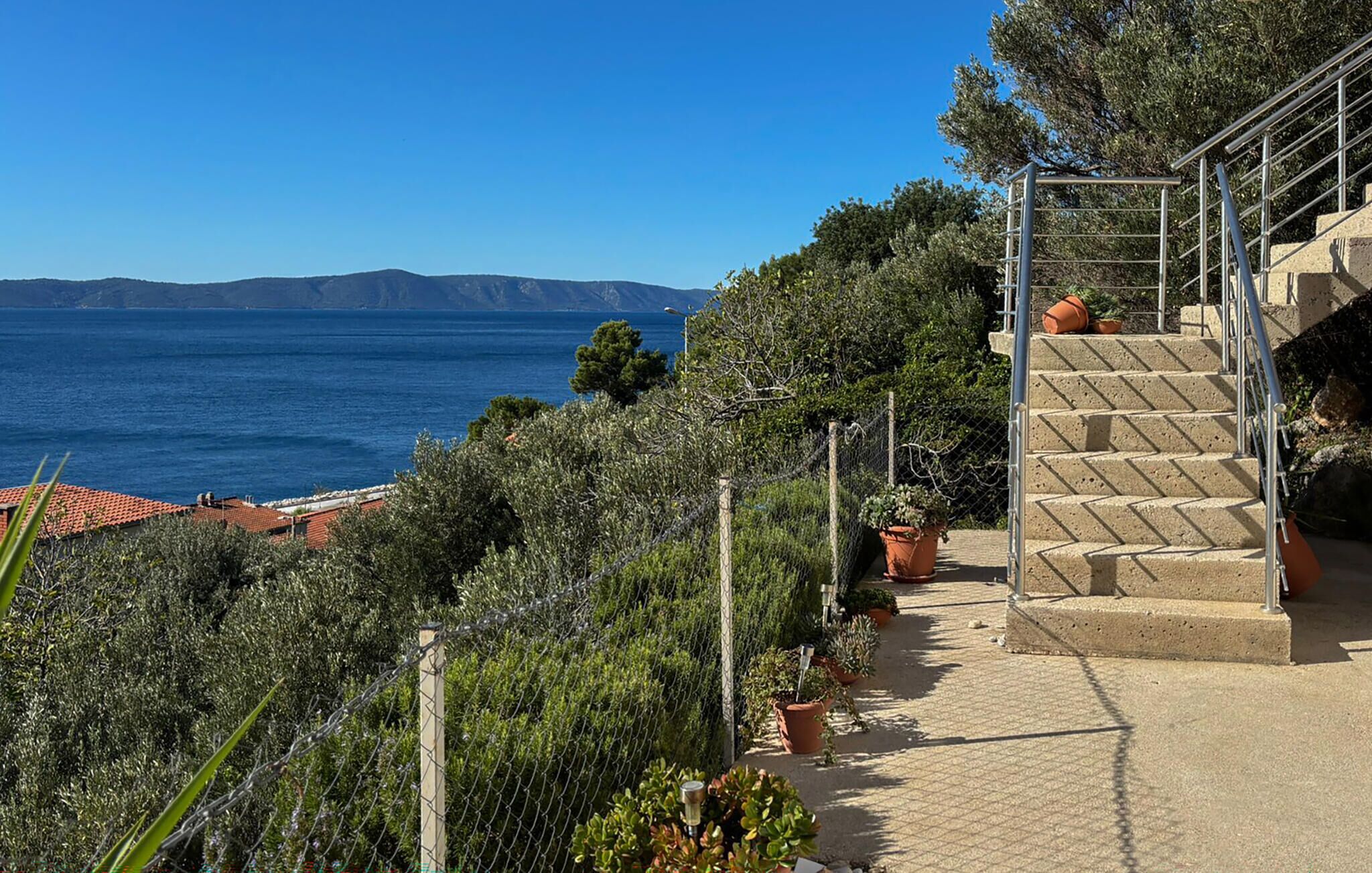 Una propiedad costera con una escalera que conduce a una terraza con vistas al mar, rodeada de vegetación y plantas en macetas.