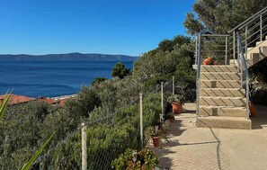 Ein Küstenanwesen mit einer Treppe, die zu einer Terrasse mit Meerblick führt, umgeben von Grünflächen und Topfpflanzen.