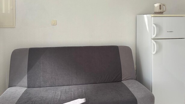 A grey sofa with a cushion, a white wall, and a white refrigerator with the brand 'TELEFUNKEN' on it. - Gorgeous apartment in Podgora with WiFi (Podgora)