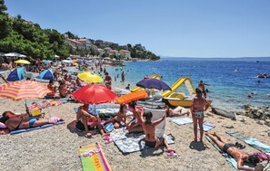 Ein überfüllter Strand mit badenden Personen, Sonnenschirmen und Booten.
