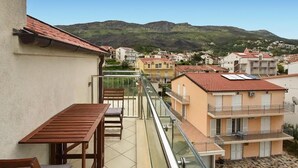 Een balkon met een tafel en stoelen, met uitzicht op een woonwijk met huizen en een berg op de achtergrond.