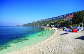 Ein Strand mit klarem Wasser, badenden Personen und Sonnenschirmen im Sand.