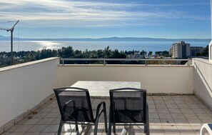 Ein Balkon mit Tisch und Stühlen, der auf ein Gewässer und ferne Berge blickt.