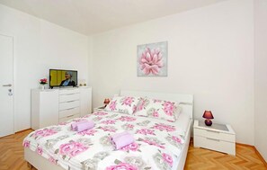 A bedroom with a bed, a television on a dresser, a nightstand with a lamp, and a floral painting on the wall. - Amazing apartment in Tucepi with lake view (Tucepi)