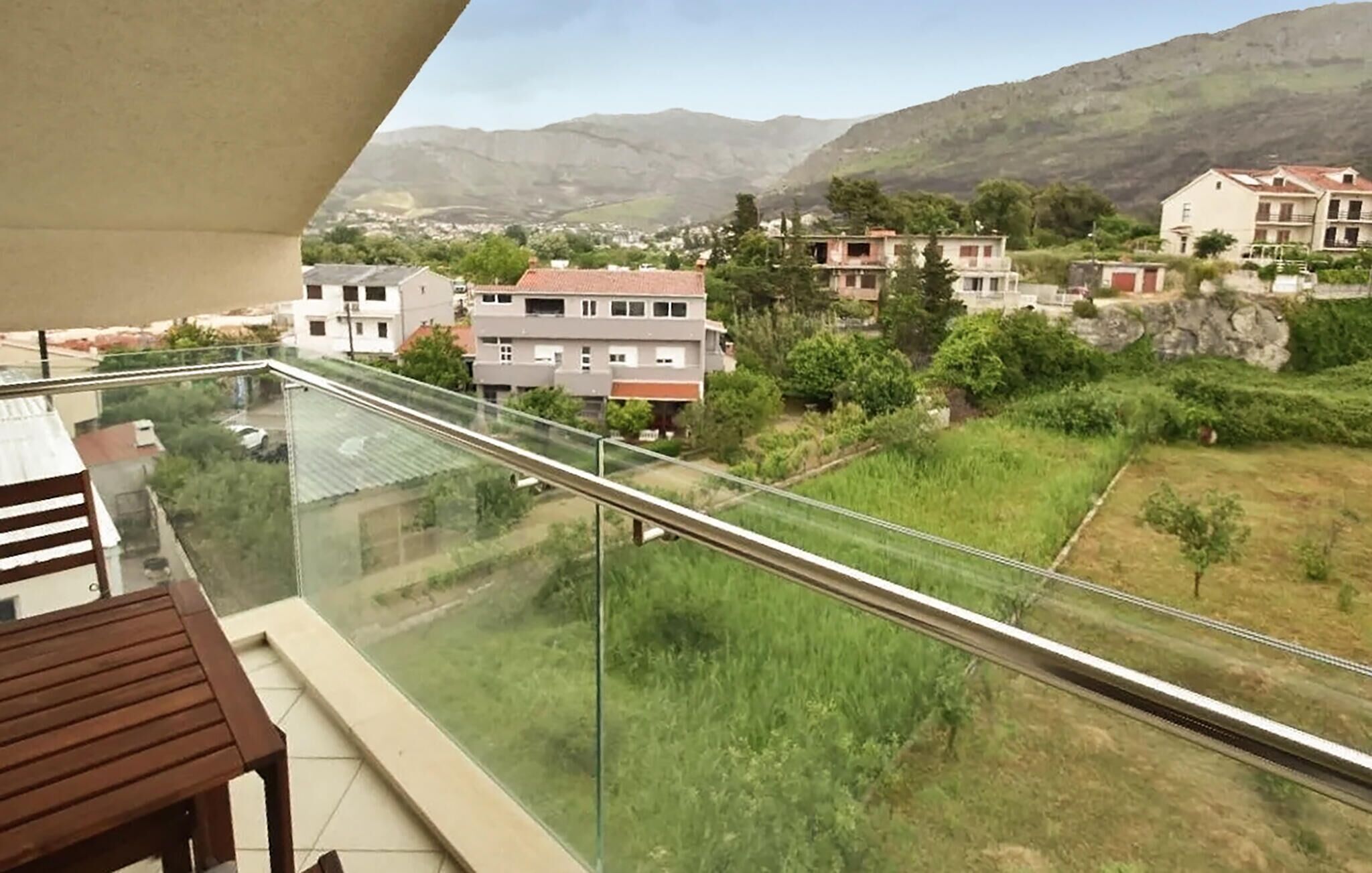 Un balcón con baranda de cristal que da a una zona residencial con casas y vegetación.