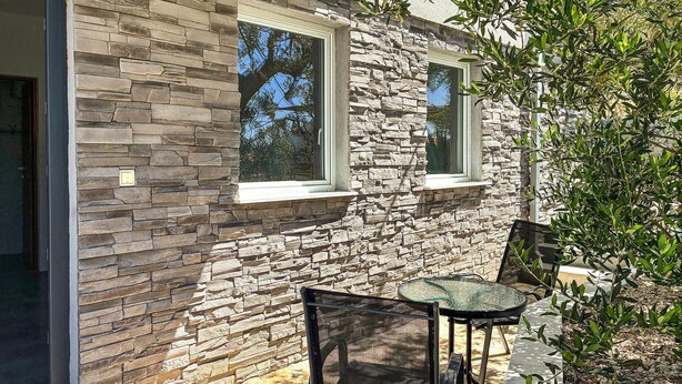 A stone exterior wall with two windows, a glass door, and a small patio area with a table and chairs. - Lovely apartment in Pisak with WiFi (Pisak)