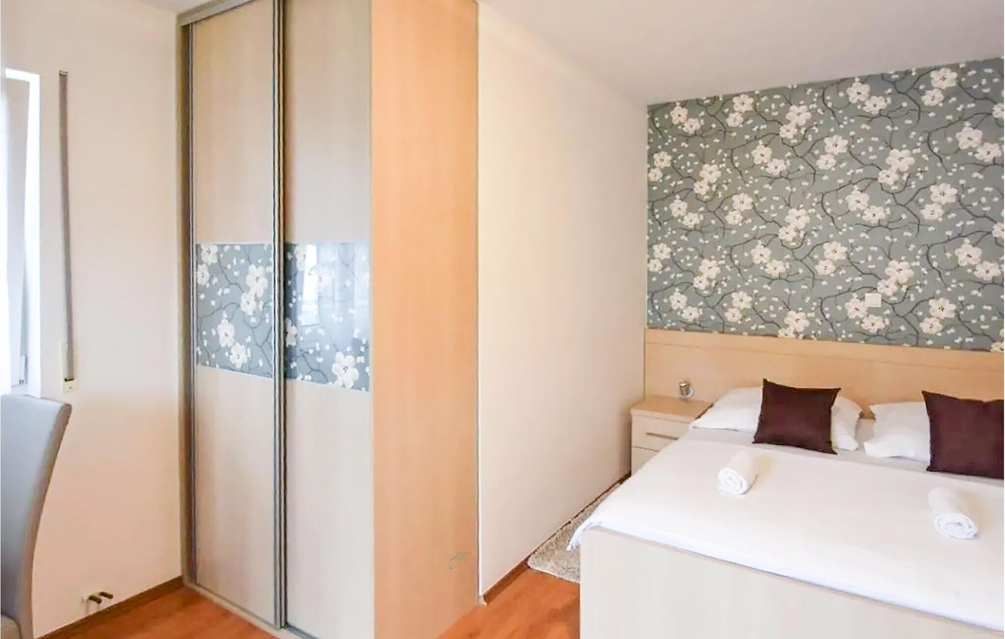A bedroom with a bed, a nightstand, a wardrobe, and a floral-patterned wall.