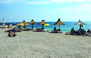 A beach with umbrellas and lounge chairs, a rocky shoreline, and a cross in the background. - Lovely apartment in Podstrana with WiFi (Podstrana)