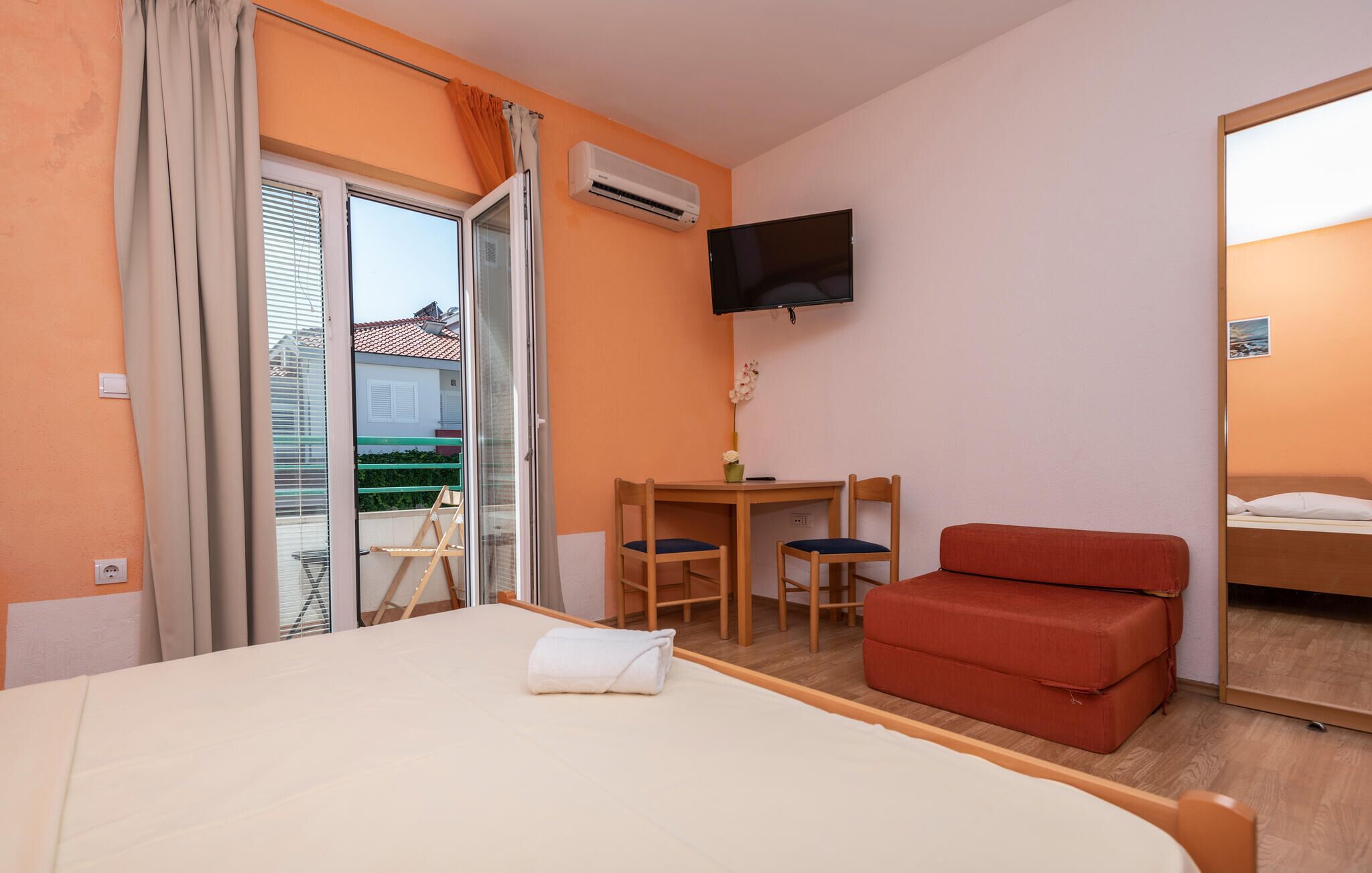 Habitación de hotel con cama, escritorio con dos sillas, televisión y balcón con cortinas.