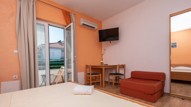 A hotel room with a bed, a desk with two chairs, a television, and a balcony with curtains. - Beautiful apartment in Makarska with WiFi (Makarska)