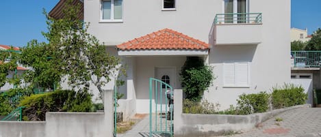 A two-story residential building with a tiled roof, a balcony, and a gated entrance.