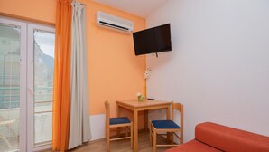 A room with a TV mounted on the wall, a small table with two chairs, a sofa, and an air conditioning unit. - Beautiful apartment in Makarska with WiFi (Makarska)