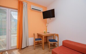 Ein Zimmer mit an der Wand montiertem Fernseher, einem kleinen Tisch mit zwei Stühlen, einer Couch und einer Klimaanlage.