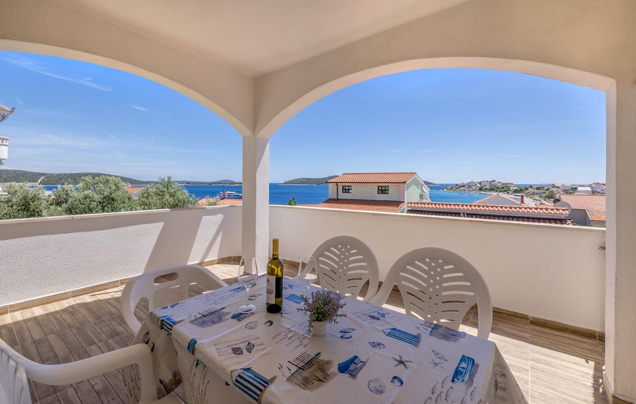 A balcony with a table set for two, overlooking a coastal view.