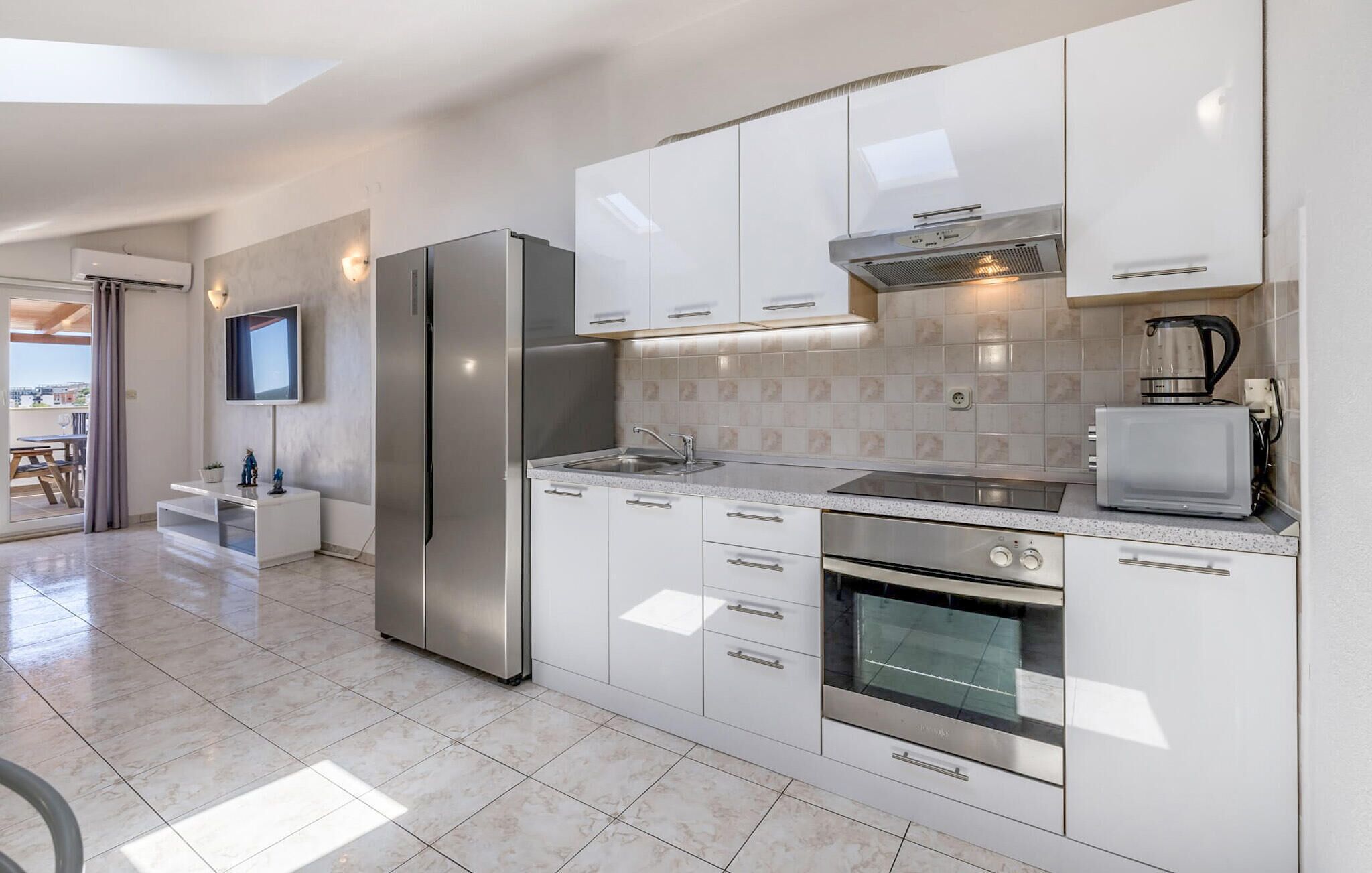 A modern kitchen with white cabinetry, stainless steel appliances, a built-in oven, and a television mounted above the counter.