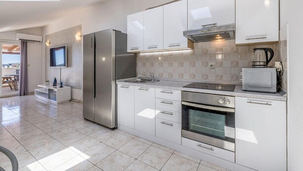 A modern kitchen with white cabinetry, stainless steel appliances, a built-in oven, and a television mounted above the counter. - Cozy home in Trogir with private swimming pool, can be inside or outside (Trogir)