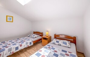 Ein kleiner, schlichter Raum mit zwei Einzelbetten, einem Nachttisch mit Lampe und einem gerahmten Bild an der Wand.