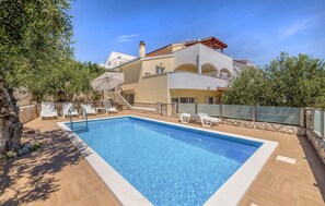 Ein zweistöckiges Haus mit Swimmingpool, Sitzgelegenheiten im Freien und einer Steinsäule.