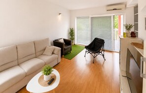 A modern living room with a sofa, a small table with a plant, a black chair, and a sliding glass door leading to an outdoor area. - 6 bedroom gorgeous apartment in Vrgorac (Vrgorac)