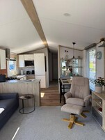 Una cocina moderna con armarios blancos, un comedor con mesa de madera y una sala de estar con sofá y sillón.
