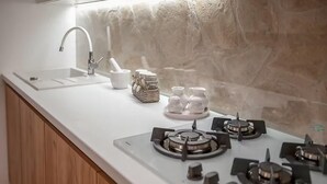Una cocina con encimera blanca, estufa a gas, lavamanos y salpicadero de piedra.