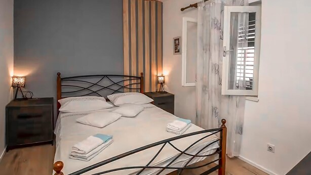 Un dormitorio con cama, mesitas de noche, una ventana con cortinas y una lámpara.