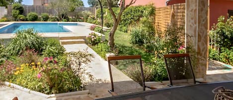 Un área de piscina con una mesa y sillas de patio, rodeada por un jardín con diversas plantas y flores.