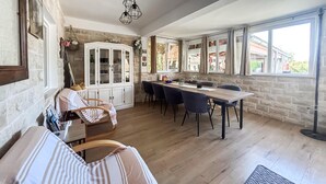 Un comedor con una mesa y sillas de madera, un armario blanco con puertas de cristal y una pared de piedra.