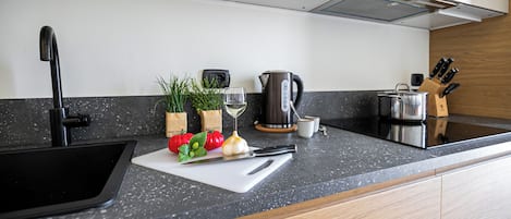 Uma cozinha moderna com uma pia preta, uma tábua de corte branca com legumes, uma chaleira e um porta-facas.