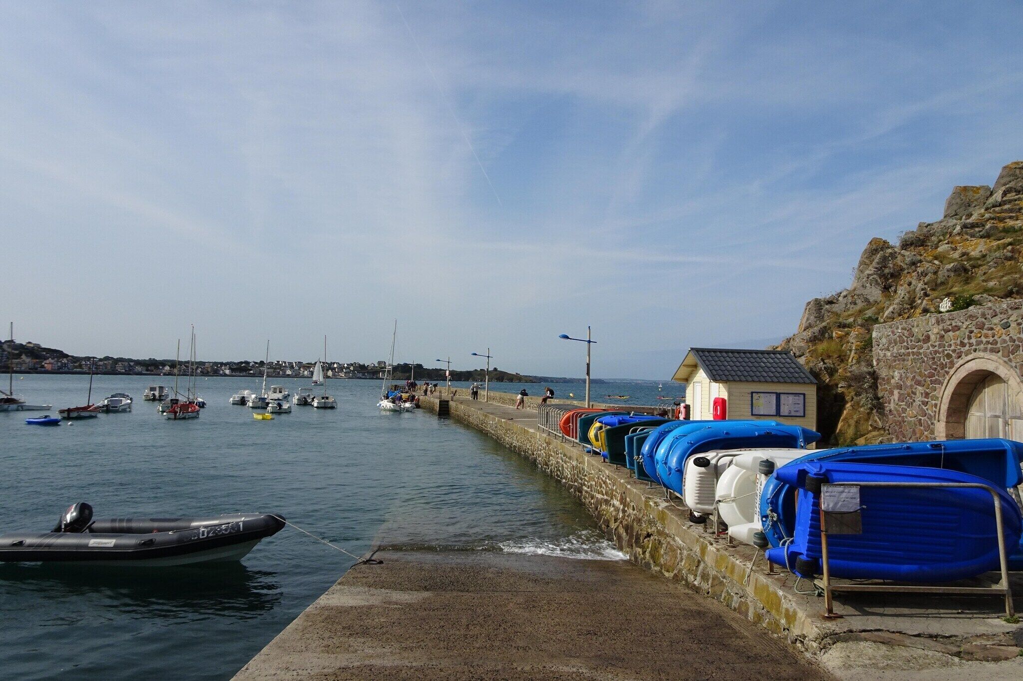 Un port avec des bateaux, un petit bâtiment et un mur de pierre.